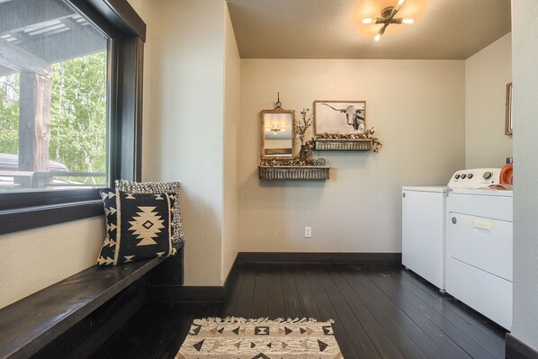 A laundry room with a washing machine, a mirror, and a shelf with decorative items.