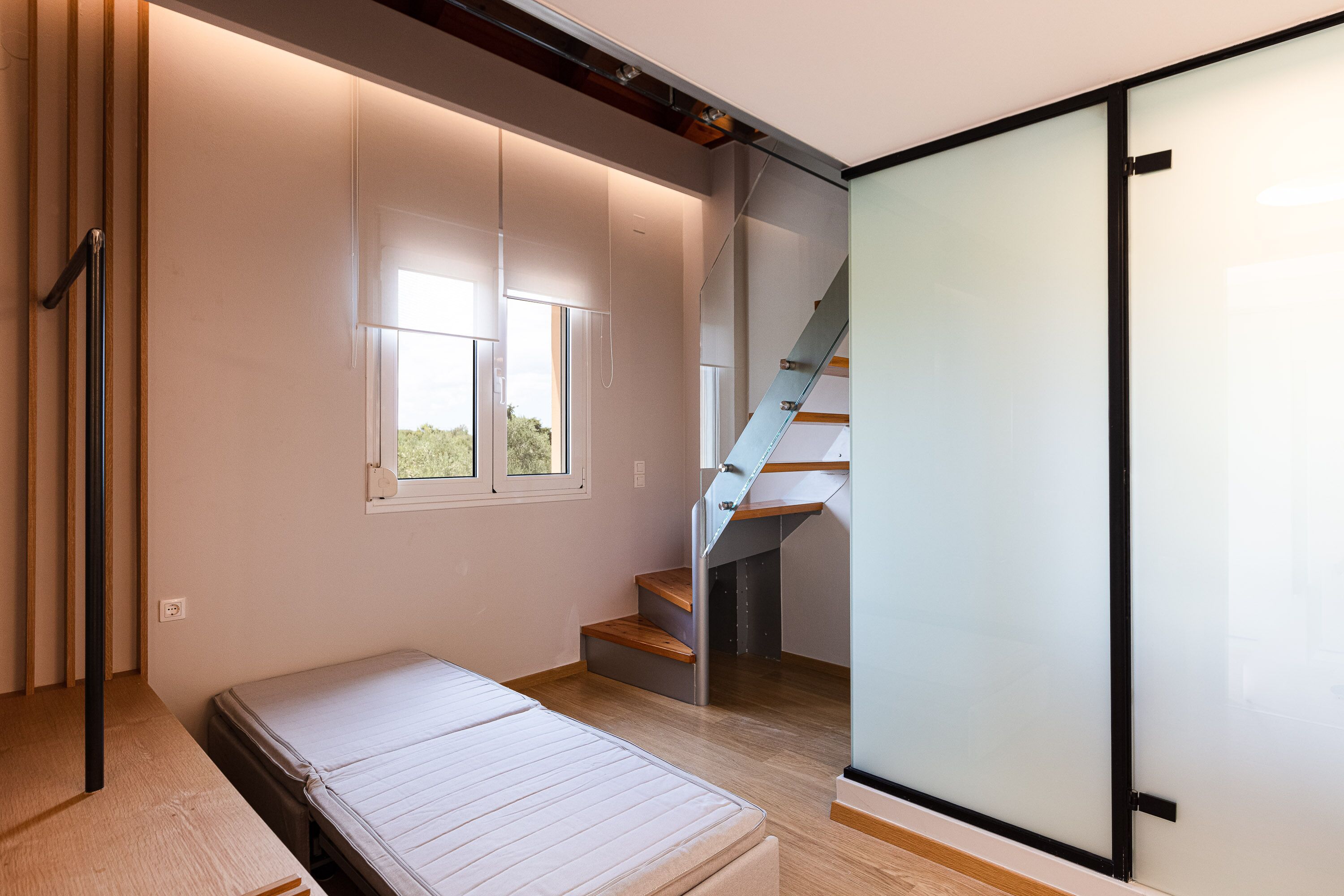 A modern bedroom with a bed, a window, and a staircase.