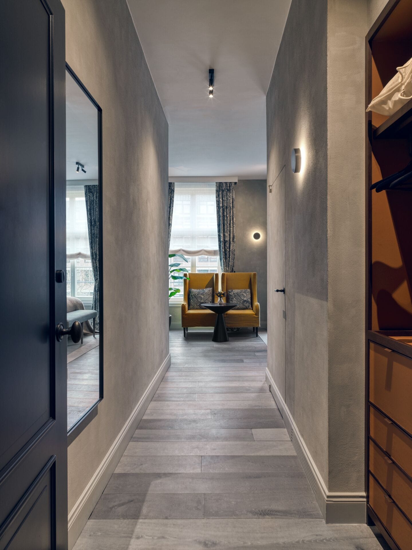 Um corredor com sofá e mesa, uma porta e uma janela com cortinas.