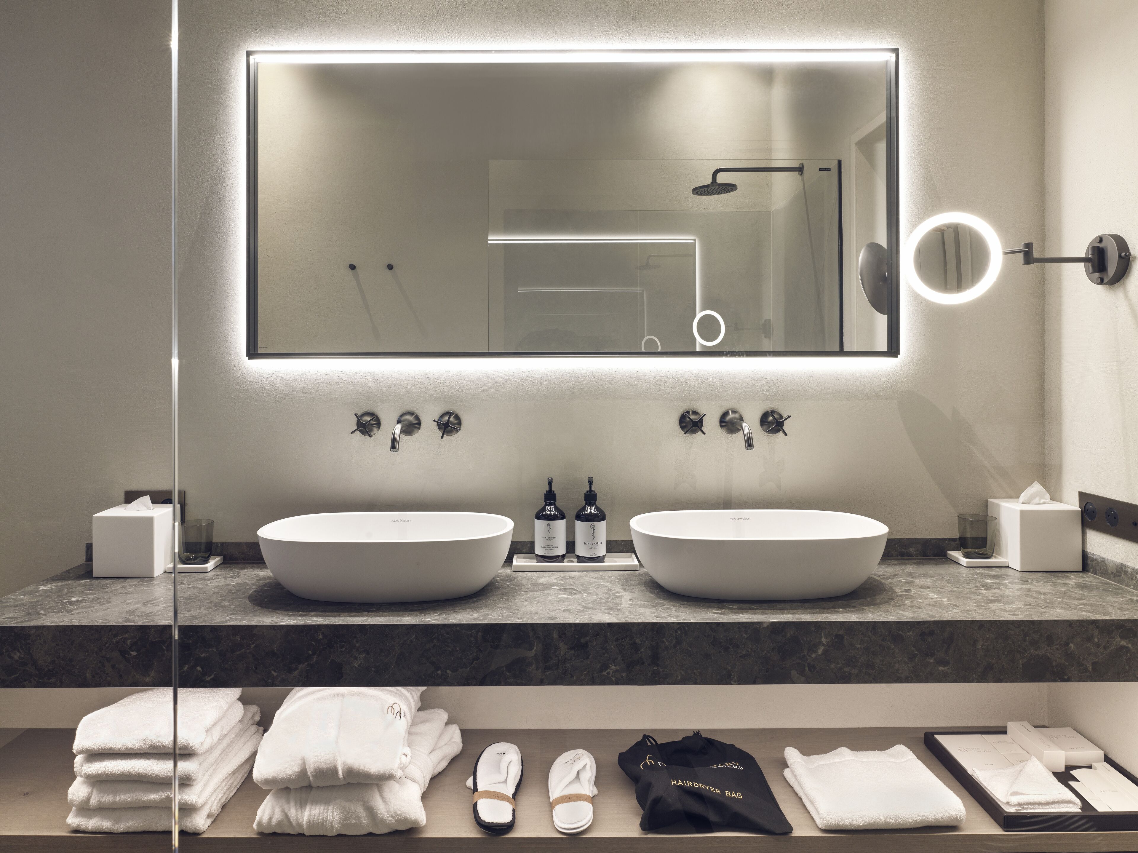 Een moderne badkamer met twee wasbakken, een grote spiegel en een badkamermeubel met toiletartikelen.