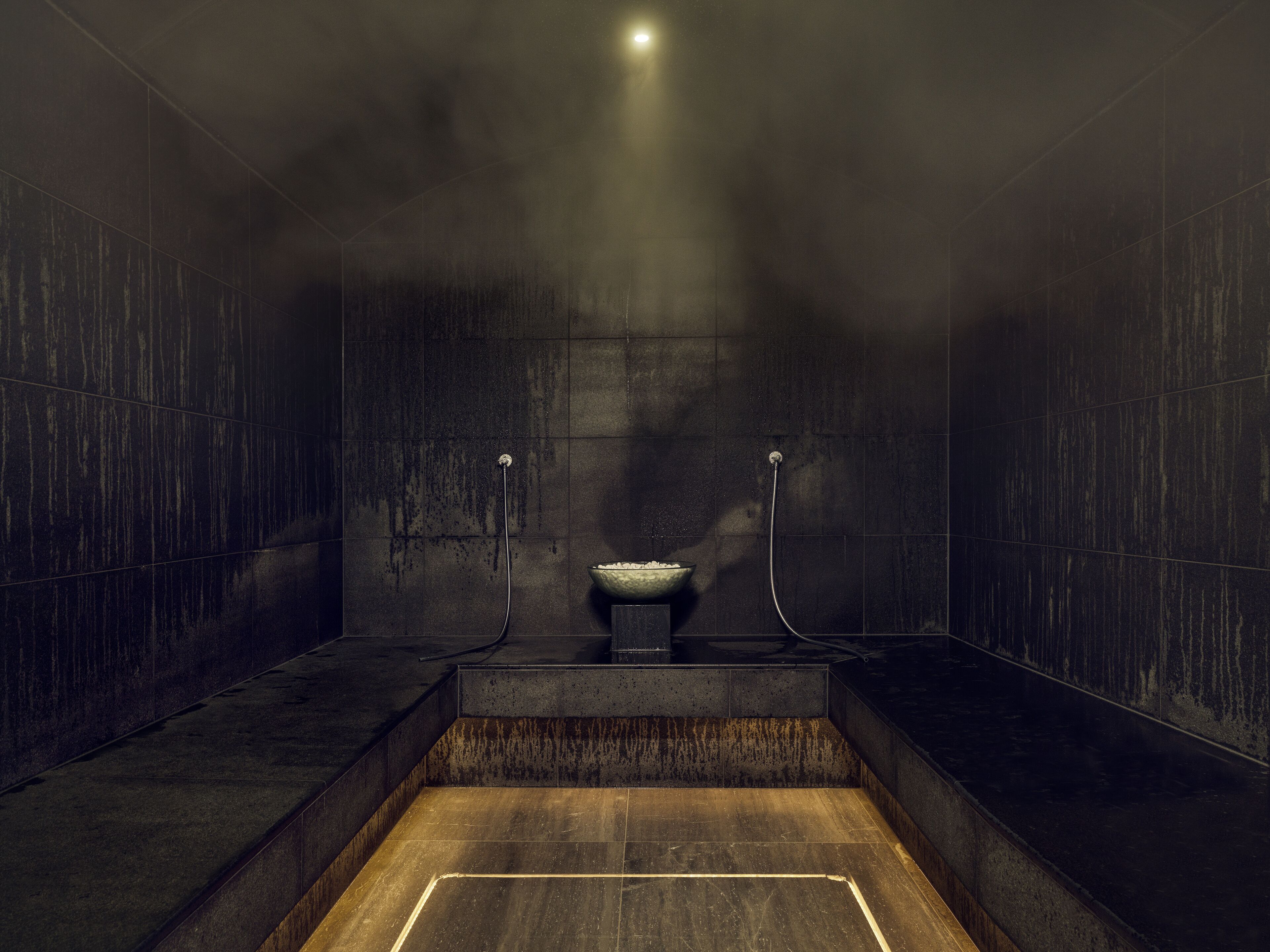 A modern, dimly lit bathroom with a large bathtub, a small sink, and a showerhead.