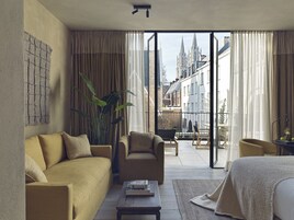A modern hotel room with a sofa, armchair, and a small table with books.