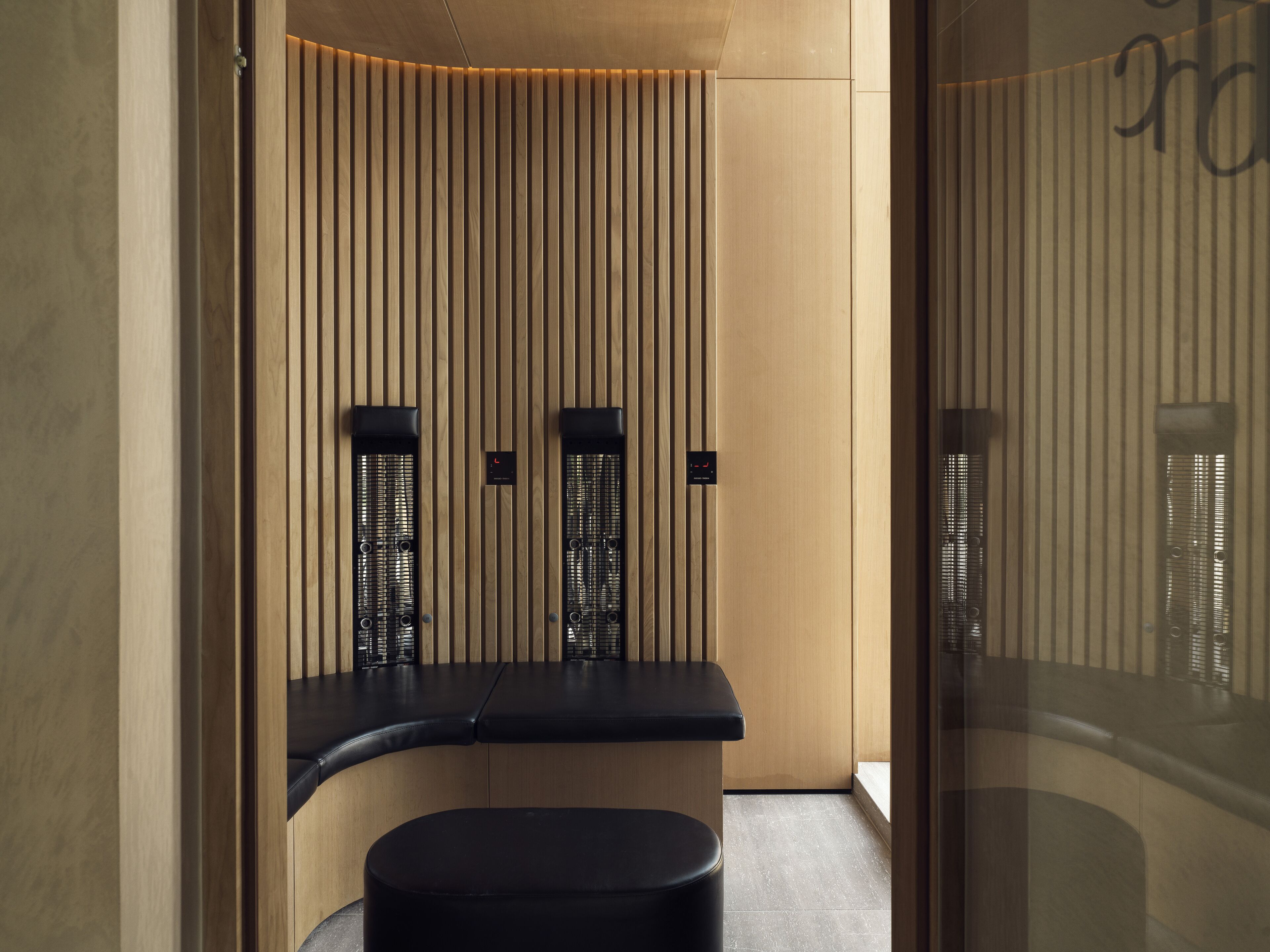 A modern, minimalist bathroom with vertical wooden slats, black fixtures, and a curved bench.
