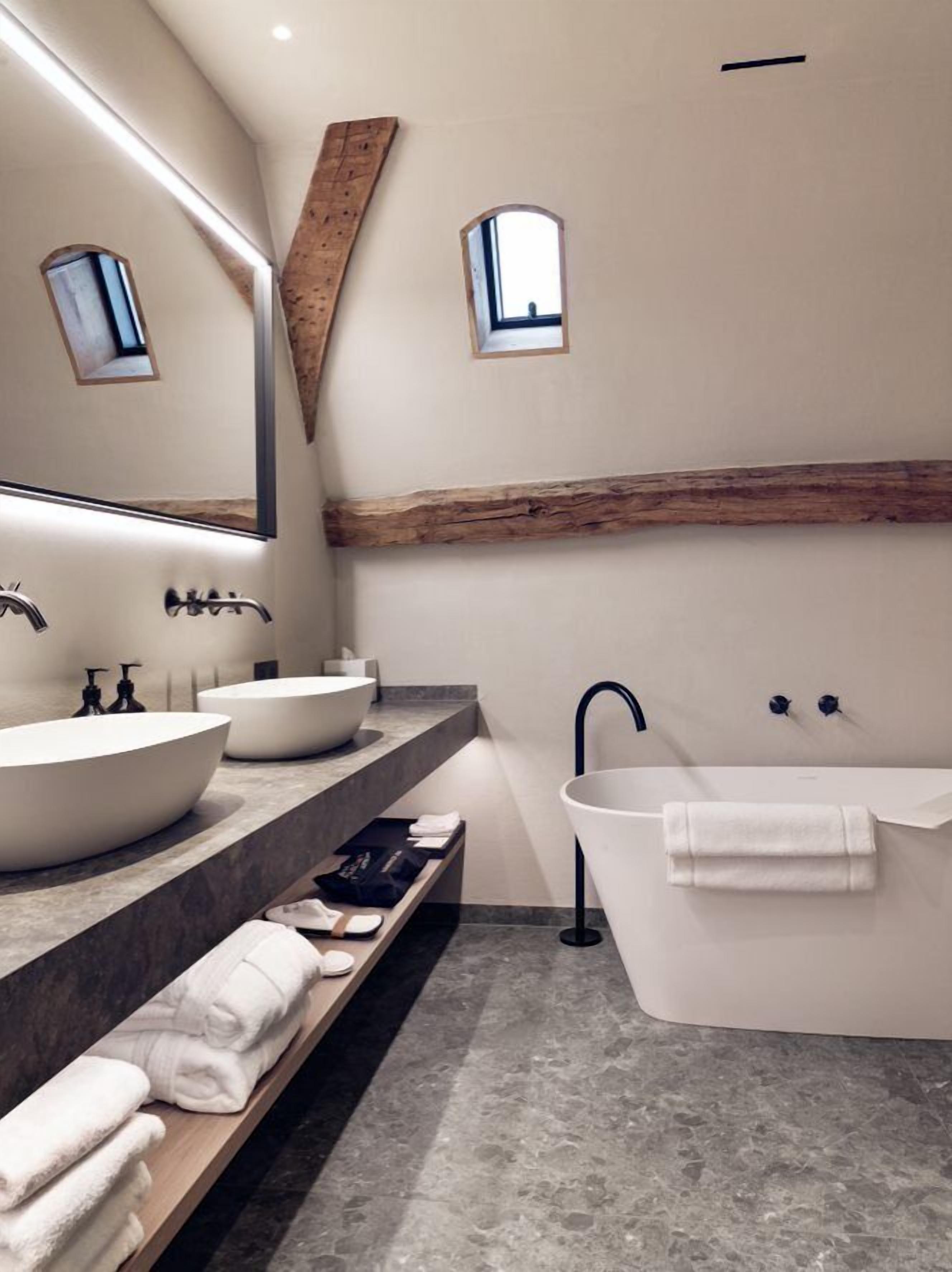 A modern bathroom with a large mirror, two sinks, a bathtub, and a wooden beam accent.