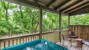 Une terrasse en bois avec un jacuzzi, des chaises et une vue sur une zone boisée.