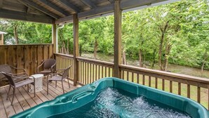 A hot tub on a wooden deck with a view of a river and trees.