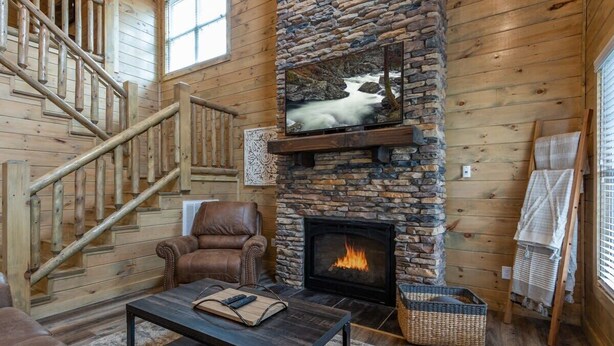 A cozy cabin interior with a stone fireplace, leather armchair, and a staircase.
