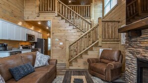 A cozy cabin interior with a wooden staircase, a stone fireplace, a leather sofa, and a coffee table.