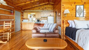 Interior acogedor de una cabaña con una mesa de comedor de madera, un sofá de cuero, una cama y una zona de cocina.