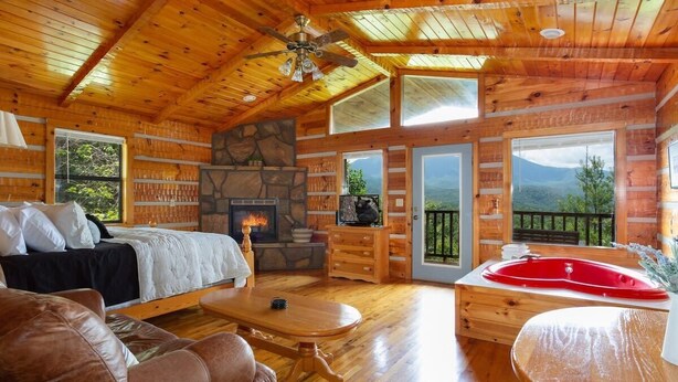 Una cabaña con chimenea de piedra, un jacuzzi rojo, muebles de madera y amplios ventanales con vistas a la montaña.