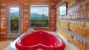 Una cabaña de madera con un jacuzzi rojo, ventanas amplias y un balcón con vistas a las montañas.