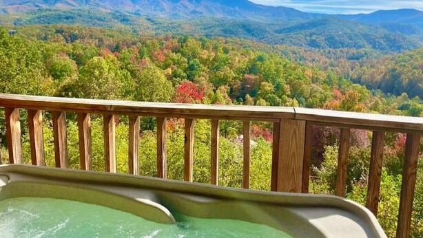 A hot tub on a wooden deck overlooking a mountainous landscape with autumn foliage.