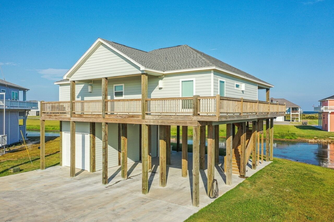 A waterfront house with a wooden deck and a covered porch.