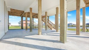 Amplio espacio interior con suelo de hormigón y vigas de madera, que incluye una escalera y ventanas grandes con vistas a un cuerpo de agua y edificios.