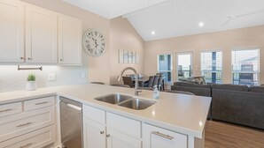 Una cocina moderna con una isla grande, armarios blancos y un comedor con un sofá gris y mesa.