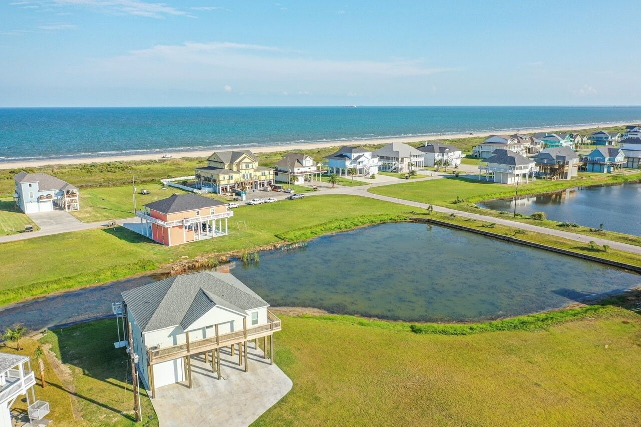 A coastal residential area with houses, a large pond, and a beach in the background.
