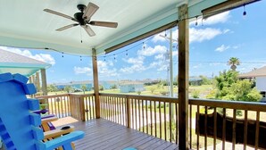 Une terrasse en bois avec un ventilateur de plafond, des sièges d’extérieur et une vue sur un quartier résidentiel.
