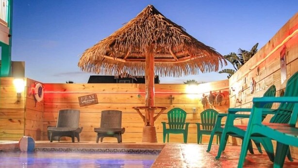 Une cabane en bois avec une piscine, des chaises et un toit de chaume.