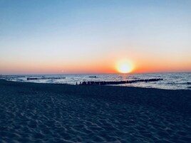 Una playa con un atardecer, olas y un muelle.