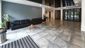 A spacious lobby with a black leather sofa, wooden coffee tables, and a striped rug. - DWIE SOSNY-Apartament na wydmie - 365PAM (Ustronie Morskie)