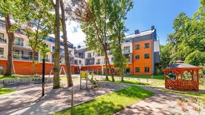 A courtyard with a playground, trees, and a building with multiple balconies. - DWIE SOSNY-Apartament na wydmie - 365PAM (Ustronie Morskie)