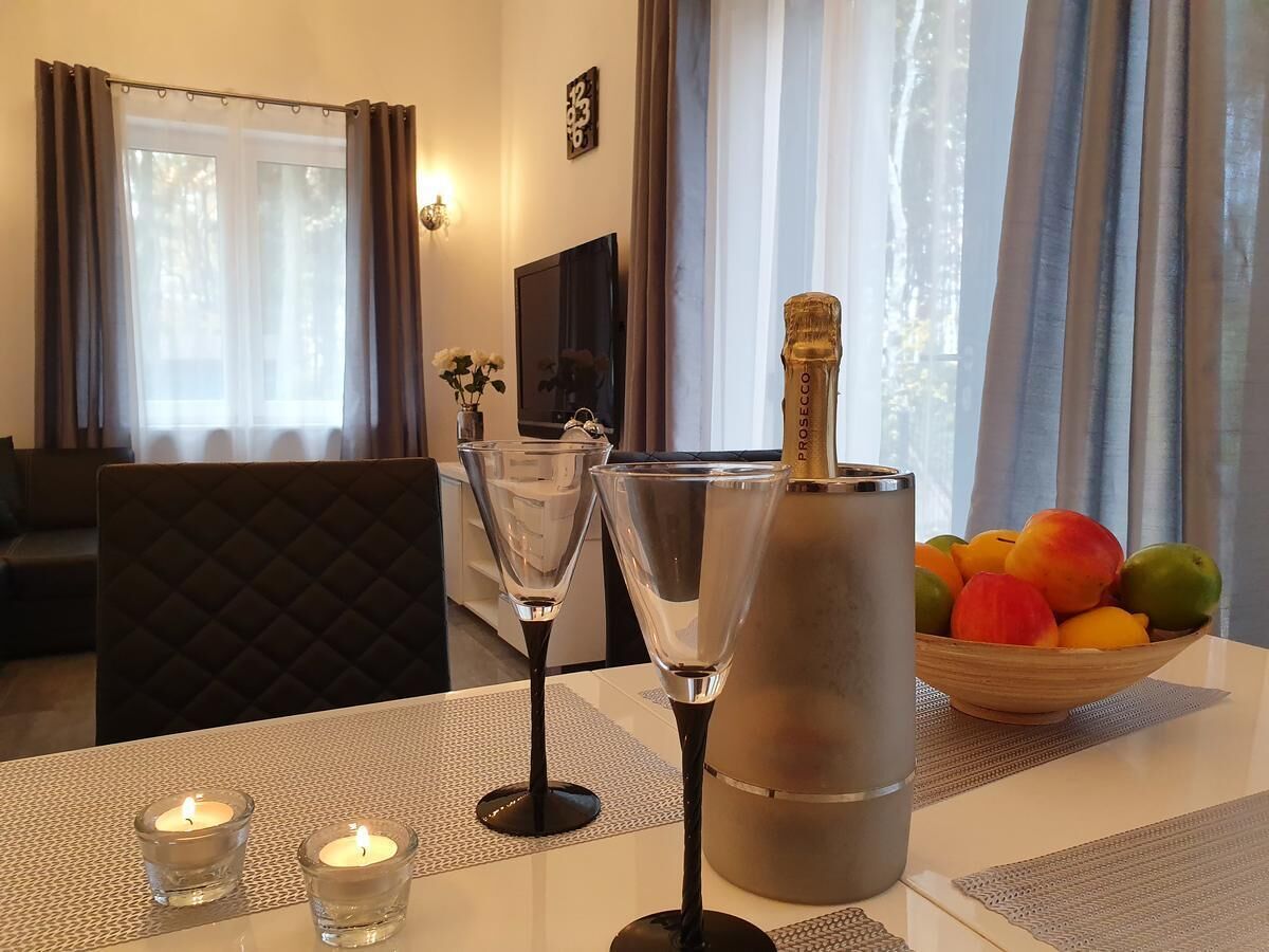 A dining table with two glasses, a candle, and a bottle of Prosecco. A bowl of fruit is on the table.