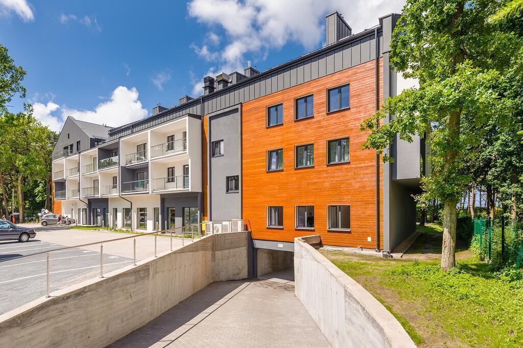 Ein modernes Mehrfamilienhaus mit mehreren Etagen, Balkonen und einem Parkplatz.