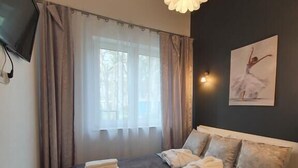 A modern hotel room with a large bed, a flat-screen TV mounted on the wall, and a painting of a ballerina. - DWIE SOSNY-Apartament na wydmie - 365PAM (Ustronie Morskie)