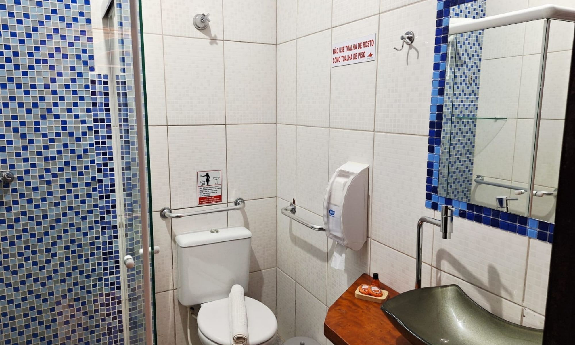 A small bathroom with a toilet, a hand dryer, and a sink. There is a sign on the wall and a mirror above the sink.