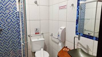 A small bathroom with a toilet, a hand dryer, and a sink. There is a sign on the wall and a mirror above the sink.