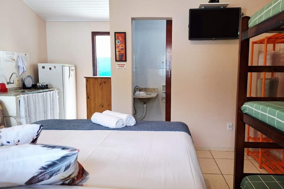 A room with bunk beds, a desk with a computer, a refrigerator, and a bathroom visible through an open door.