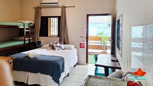 Habitación de hotel con literas, una cama individual, un escritorio con silla, una mesita pequeña, una planta en maceta y una puerta que da a un espacio exterior.