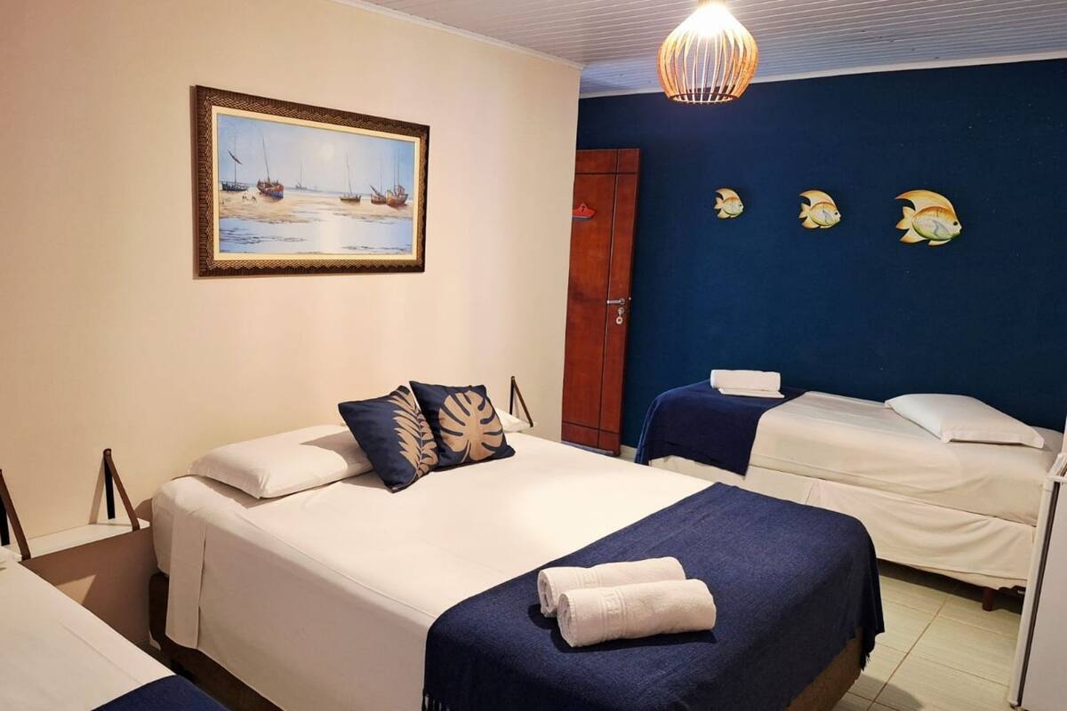 A hotel room with a bed, a smaller bed, a painting of boats on the wall, and a door.