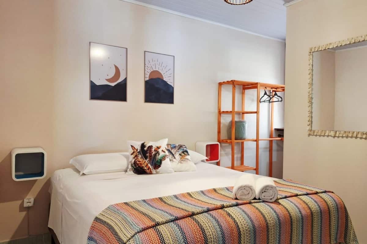 A hotel room with a bed, a TV, a mirror, and two wall art pieces depicting a moon and a sun.