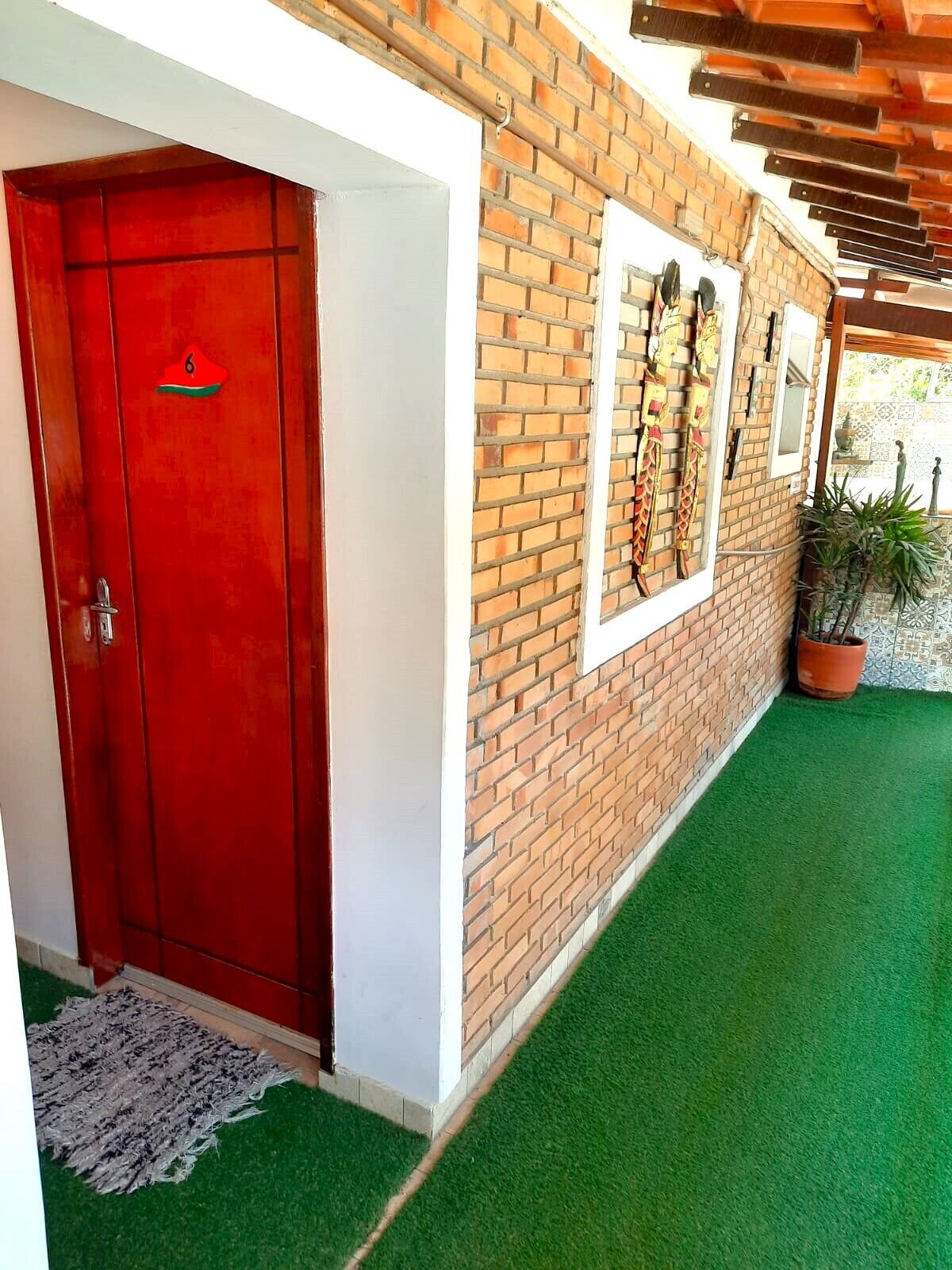 A red door with a number, a brick wall with windows, and a green artificial lawn.