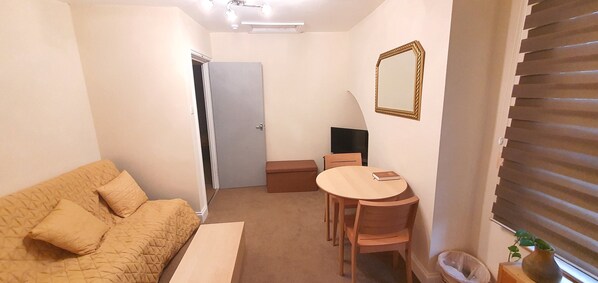 A compact living space with a sofa, a small table, and a TV. - Grace Apartments - Living Waters 1 (Ashford)