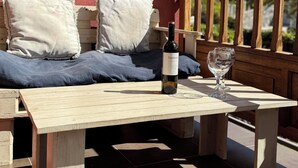 A wooden table with a bottle of Tajin wine and a glass, set on a terrace with a red wall and a wooden railing. - Luxury apartment in Residencial El Mocan (Palm-Mar)