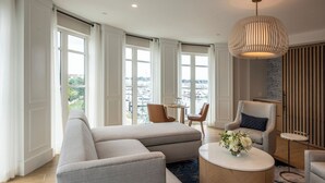 Uma sala de estar moderna com um amplo sofá modular, uma mesa de centro redonda e vista para a cidade através de grandes janelas.