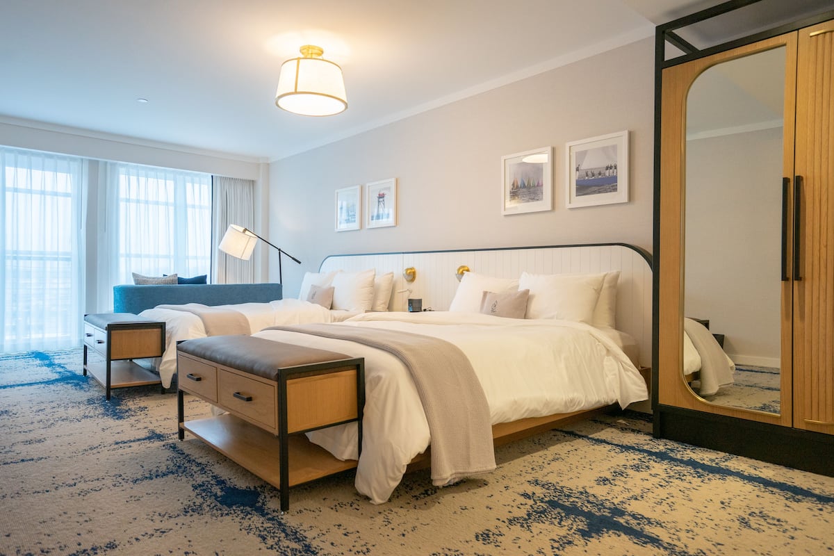 A modern hotel room with a large bed, bedside tables, a wardrobe, and a large mirror.