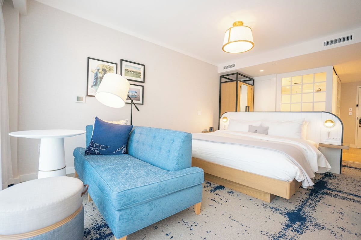 A hotel room with a blue sofa, a bed with white bedding, a small white table, and a lamp.