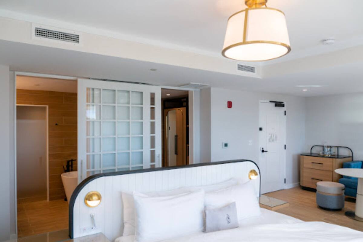 A modern hotel room with a large bed, a bedside table, a wardrobe, and a bathroom visible through an open door.