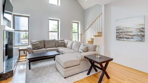 A spacious living room with a large L-shaped sectional sofa, a fireplace, and a staircase leading to an upper level. - 3 Flat Building Downtown - With Private Patios (Chicago)