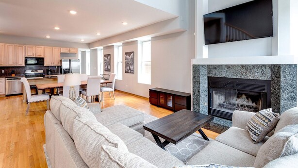 A spacious living area with a fireplace, a dining table with chairs, and a kitchen in the background. - 3 Flat Building Downtown - With Private Patios (Chicago)