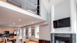 A spacious living area with a high ceiling, a fireplace, a flat-screen TV, and a dining area with a kitchen in the background. - 3 Flat Building Downtown - With Private Patios (Chicago)