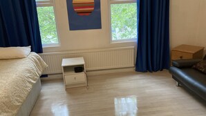 A bedroom with a bed, a nightstand, a dresser, a window with curtains, and a radiator.