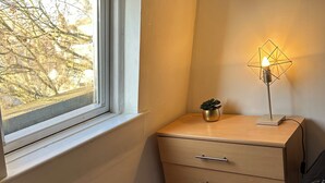 A room with a window, a wooden dresser with drawers, and a table.