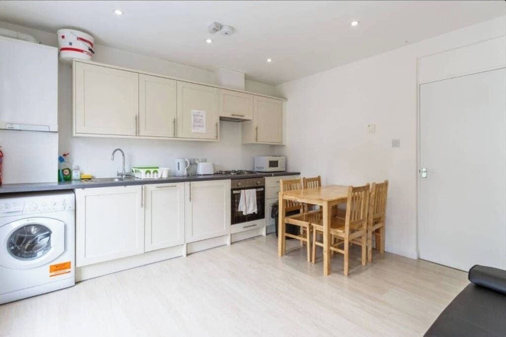 A compact kitchen with white cabinets, a microwave, a sink, and a wooden dining table.