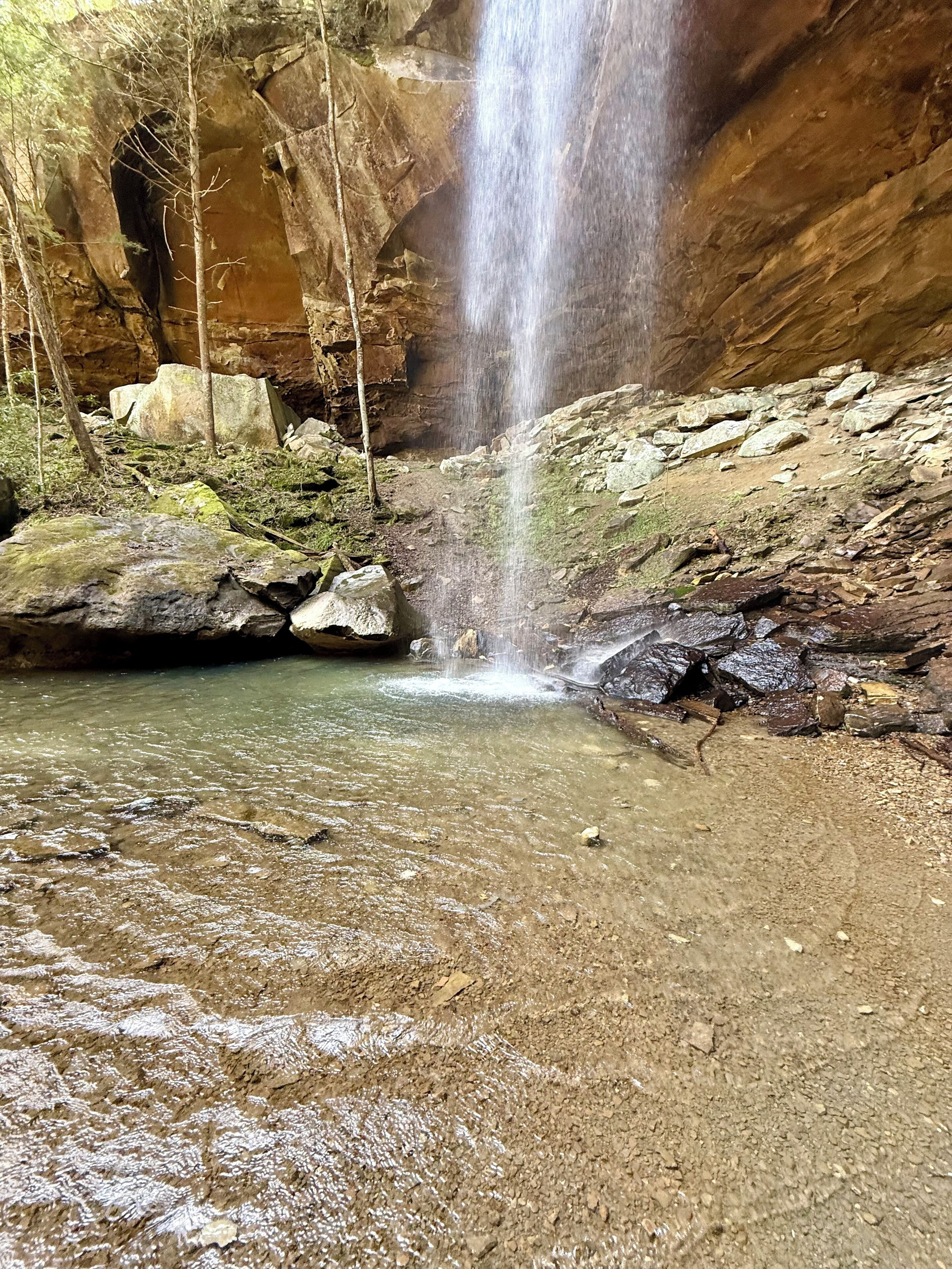 A natural waterfall in a rocky cave with clear water and moss-covered rocks.
