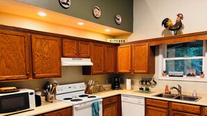 A kitchen with wooden cabinets, a stove, a microwave, a sink, and a window with a view of trees.