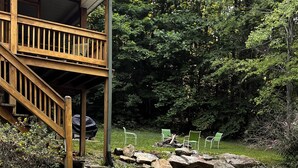 A wooden deck with a staircase leading to a covered area, surrounded by greenery and outdoor seating.